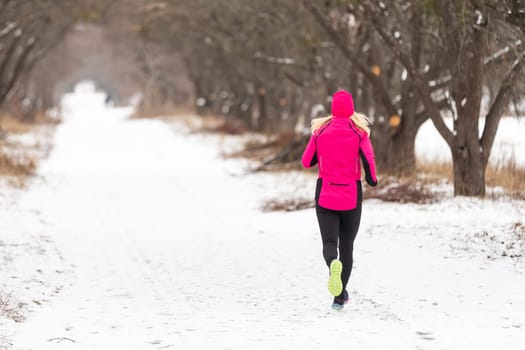 Winter running in park: happy woman runner jogging in snow, outdoor sport and fitness concept . High quality photo