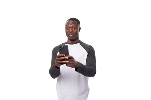 a young American guy with a short haircut dressed in a long-sleeve sweater looks in surprise at the screen of a smartphone.