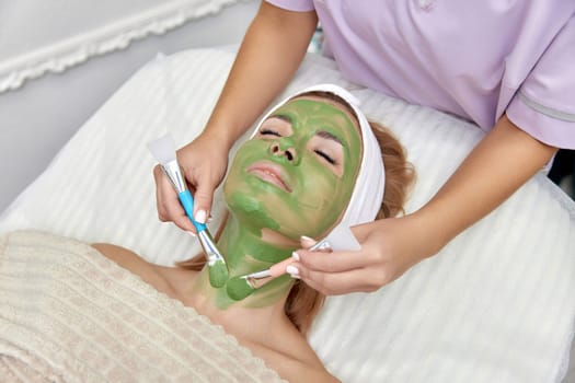 female beautician applies the mask to the face of beautiful woman in the spa salon. facial skin care