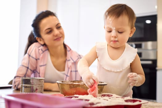 mother and little baby girl preparing the dough in the kitchen, bake cookies. happy time together