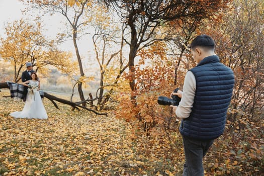 Professional wedding photographer taking pictures of the bride and groom in nature in autumn