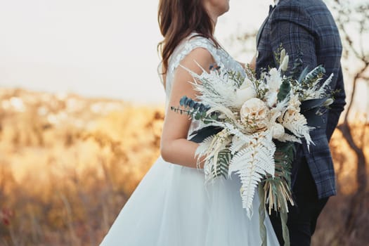 bride and groom holding beautiful bouquet in nature in autumn