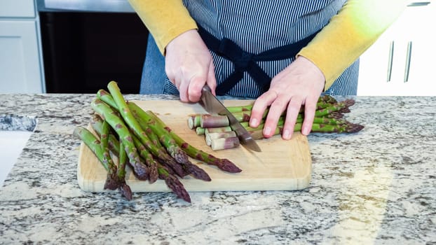 Large organic asparagus stalks are being sliced in a modern white kitchen, in preparation for steaming.