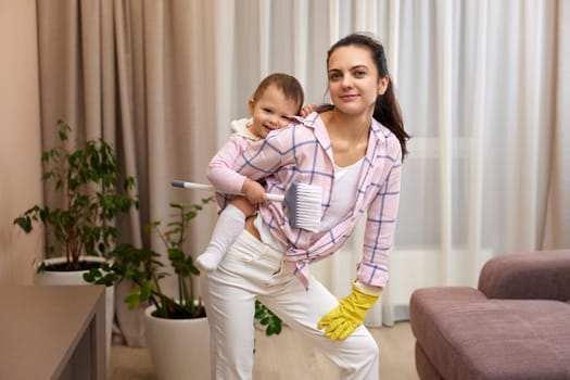 happy mother housewife is holding cute baby girl and doing housework at home, Happy family having fun
