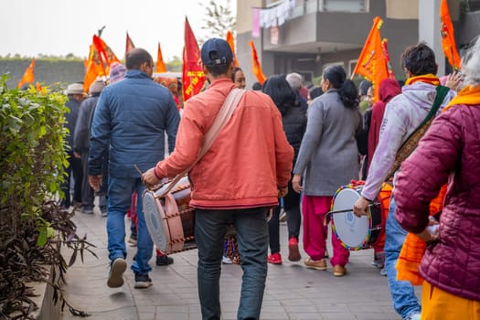 Ayodhya, Uttar Pradesh, India - 22nd Jan 2024: Dhol drummer walking along with hindu devotees on shobha yatra holding saffron flags celebrating Ram Mandir temple consecration in India