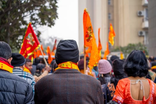 Ayodhya, Uttar Pradesh, India - 22nd Jan 2024: Focus blur shot showing back of old man wearing winter clothes and bhagwa saffron scarf walking with crowd carrying flag celebrating the Pran Pratishtha consecration of Ram mandir temple