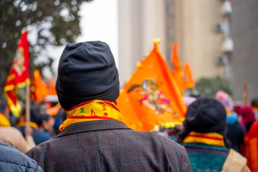 Ayodhya, Uttar Pradesh, India - 22nd Jan 2024: Focus blur shot showing back of old man wearing winter clothes and bhagwa saffron scarf walking with crowd carrying flag celebrating the Pran Pratishtha consecration of Ram mandir temple