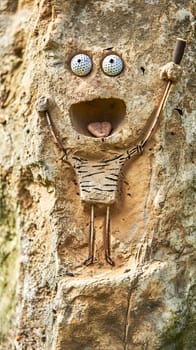 figure embedded in a rock face, with golf ball eyes, a gaping mouth, and holding a golf club, giving a humorous and playful touch to an otherwise natural and rugged surface. vertical