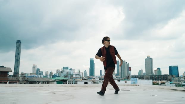 Motion shot of B-boy dance performance by professional street dancer at rooftop with sky scrapper, city view. Attractive asian hipster show energetic footstep. Outdoor sport 2024. Endeavor.