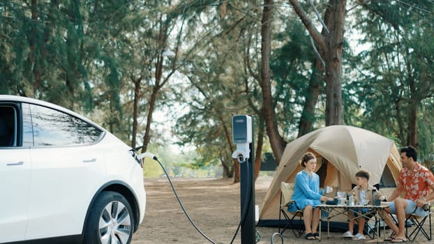 Outdoor adventure and family vacation camping in nature travel by eco friendly car for sustainable future. Lovely family recharge EV car with EV charging station in campsite. Perpetual