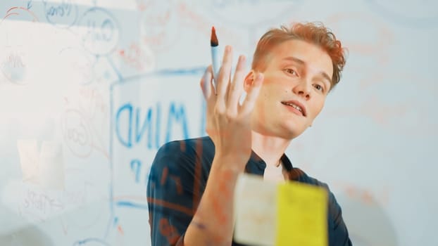 Closeup image of professional caucasian businessman presenting business idea with confident while writing and drawing mind map on glass board by using mind map and colorful sticky note. Immaculate.