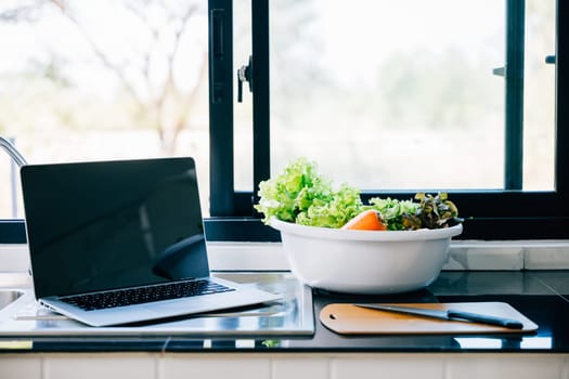 An open laptop with an empty screen against a background of healthy vegetables illustrating the concept of online grocery shopping apps and cookbooks focused on nutritious recipes and diet plans.