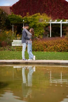 A couple in love hugs on the shore of a city pond in the European town. love story against the backdrop of autumn nature. romantic ambiance, couple goals, outdoor romance, seasonal charm, love in the city, autumnal vibes, European town, city pond, affectionate bonding, love story