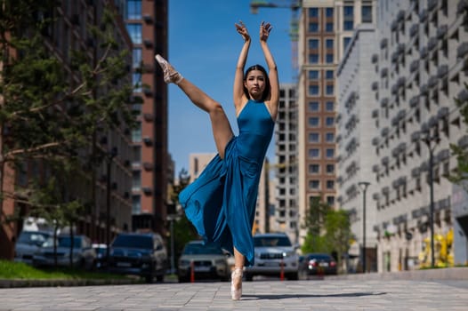 Beautiful Asian ballerina in blue dress posing in splits outdoors. Urban landscape