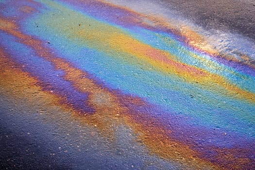 Spots of oil or gasoline are scattered randomly on the asphalt after rain. Abstract background close-up