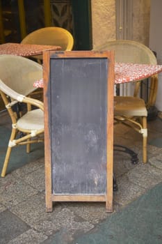 Empty wooden blackboard mockup standing outdoors in front of cafe .