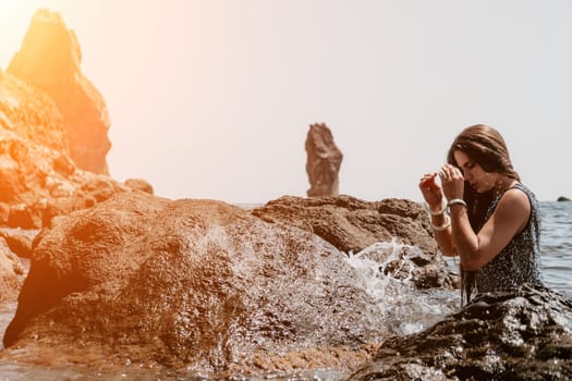 Woman travel sea. Young Happy woman in a long red dress posing on a beach near the sea on background of volcanic rocks, like in Iceland, sharing travel adventure journey