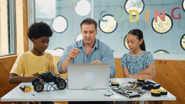 Front view of smart handsome teacher explain electronic equipment by using laptop with car model. Multicultural children listen teacher explain about car model structure in STEM class. Edification.