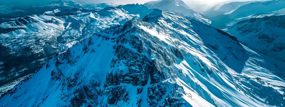 Aerial view of snow-covered mountain peaks with sharp ridges and deep valleys under a clear blue sky
