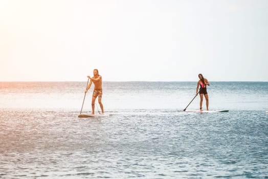 Sea woman and man on sup. Silhouette of happy young woman and man, surfing on SUP board, confident paddling through water surface. Idyllic sunset. Active lifestyle at sea or river