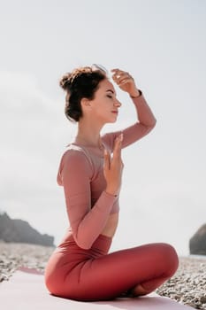 Young woman with long hair in white swimsuit and boho style braclets practicing outdoors on yoga mat by the sea on a sunset. Women's yoga fitness routine. Healthy lifestyle, harmony and meditation