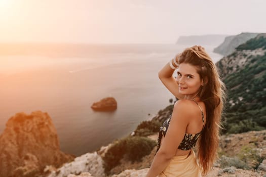 Woman travel sea. Happy tourist taking picture outdoors for memories. Woman traveler looks at the edge of the cliff on the sea bay of mountains, sharing travel adventure journey.