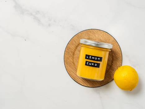 Delicious homemade lemon curd. Glass jar with lemon curd on white marble background. Black sticky label with text Lemon Curd on jar. Top view or flat lay. Copy space