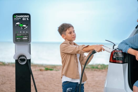 Family road trip vacation traveling by the beach with electric car, mother and son recharge EV car with green and clean energy. Family natural travel with eco-friendly car. Perpetual