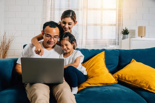 In their cozy home parents and children gather on the couch with a laptop connecting through modern technology. It's a portrait of a happy family sharing smiles and togetherness.