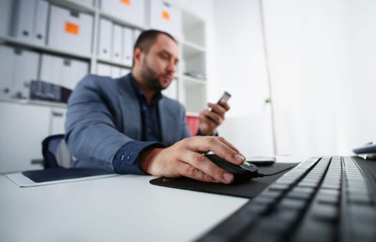 businessman work on computer hold mouse in arm and mobile phone in other closeup office worker concept