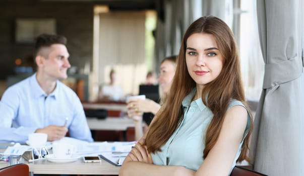 Beautiful smiling cheerful girl at cafe look in camera with colleagues group in background. White collar worker at workspace job offer modern lifestyle client visit profession train concept