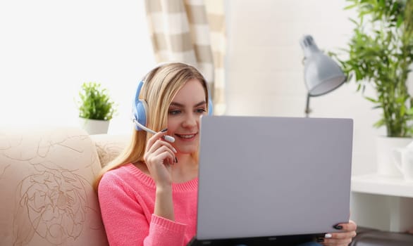 young beautiful blond woman sit on the sofa in livingroom hold laptop in arms listen to music sunny morning concept