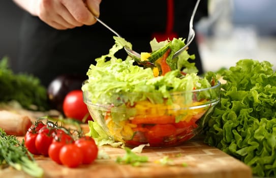 Cook holds fork in hand and mixes salad fresh vegetables seasoned with olive oil. Raw food and vegetarian in modern society is popular concept.