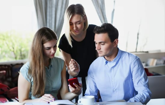 A group of people in a cafe communicate with a cup of coffee looking at the smartphone app and photos from the vacation