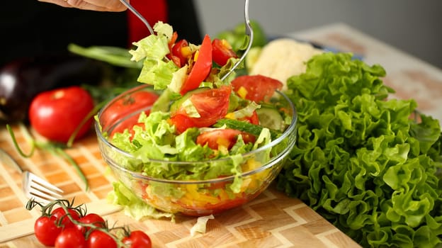 Cook holds fork in hand and mixes salad fresh vegetables seasoned with olive oil. Raw food and vegetarian in modern society is popular concept.