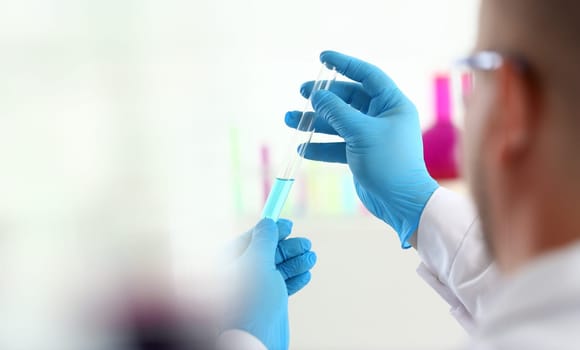 A male chemist holds test tube of glass in his hand overflows a liquid solution of potassium permanganate conducts an analysis reaction takes various versions of reagents using chemical manufacturing.