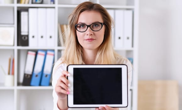 Beautiful businesswoman wearing glasses portrait at the office holding a tablet in hand sitting at the table smiling and looking at the camera teacher expresses success checking the test papers.