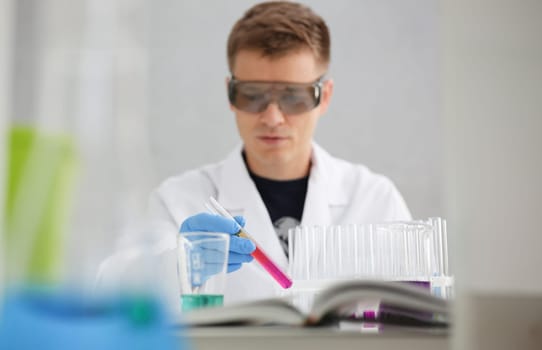 A male chemist holds test tube of glass in his hand overflows a liquid solution of potassium permanganate conducts an analysis reaction takes various versions of reagents using chemical manufacturing.