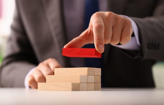Male hand holds red wood block of stair finish next step rare progress personnel talent authority hot pyramid background on ladder different insurance concept closeup