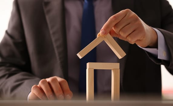 Male hand holds the roof to the lock in the hand against the backdrop of the toy house sale purchase lease concept real estate services on the market.
