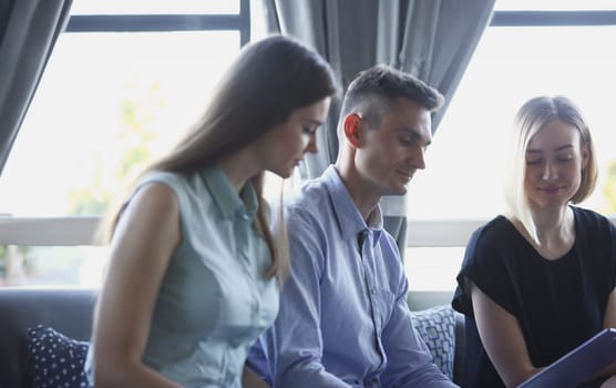 Three young business people in a cafe discussing the problem of teamwork is holding a clipboard look smiles and laughing lifestyles are examining documents and laptop.