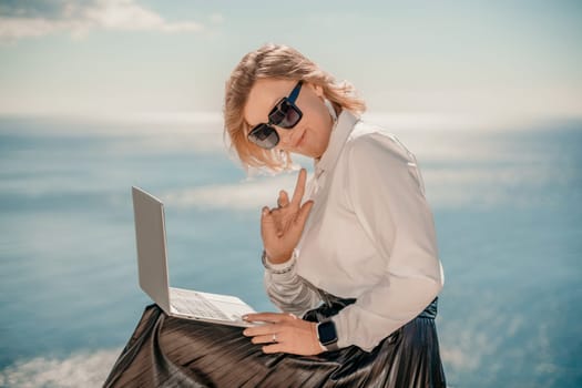 Business woman on nature in white shirt and black skirt. She works with an iPad in the open air with a beautiful view of the sea. The concept of remote work