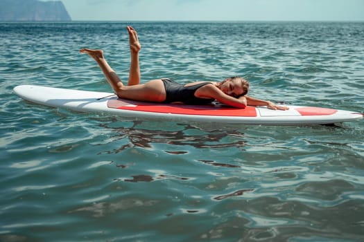 Woman sap sea. Sports girl on a surfboard in the sea on a sunny summer day. In a black bathing suit, he lies on a sap in the sea. Rest on the sea