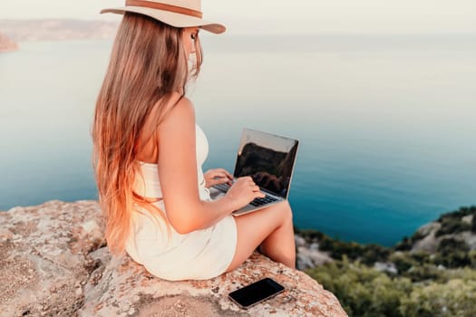 Freelance women sea working on the computer. Good looking middle aged woman typing on a laptop keyboard outdoors with a beautiful sea view. The concept of remote work