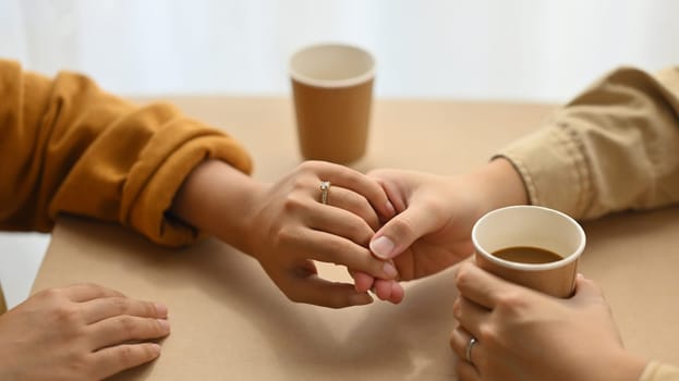Close up of married couple holding hands while sitting together in cafe with coffee cups. Love, relationship and lifestyle concept.