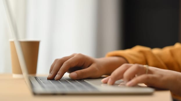 Woman hands typing on laptop keyboard while working online at home. Closeup.