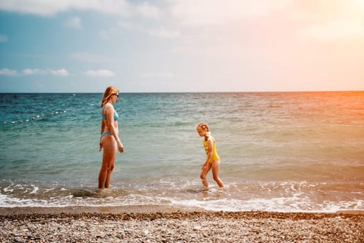 Happy loving family mother and daughter having fun together on the beach. Mum playing with her kid in holiday vacation next to the ocean - Family lifestyle and love concept.