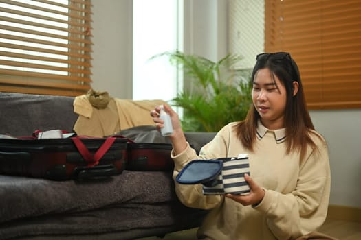 Happy young woman packing suitcase in living room getting ready for trip.