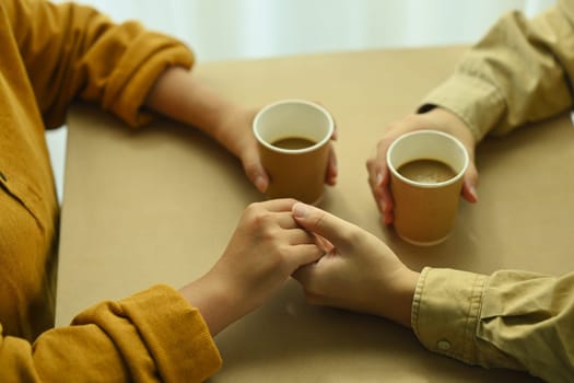 Top view of young lovers having a coffee time while holding hands. Love, relationship and lifestyle concept
