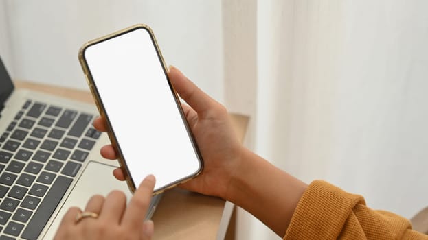 Woman using mobile phone in front of laptop at desk. Empty screen for advertising or message.